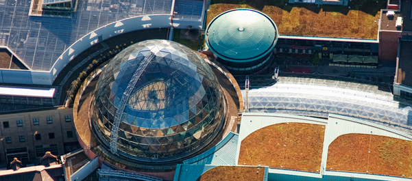 Aerial view of a large roof structure with a green roof and glazed dome, showing the scale of rubber waterproofing systems used on major buildings
